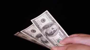 Hand Holding Three 100 Dollar Bills on Isolated Black Background. Concept of money, savings, payments, purchases, investments. Wealth. Business and finance. Copy space. Receiving profit, salary.