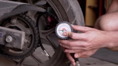 Motosiklet lastiğindeki hava basıncını basınç göstergesi ile kontrol eden bir adam. Basınç manometresi lastik basıncını ölçer. Şoför garajda, ayrılmadan önce motosiklet tekerlerinin güvenliğini kontrol ediyor.