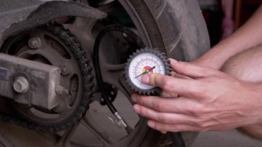 Motosiklet lastiğindeki hava basıncını basınç göstergesi ile kontrol eden bir adam. Basınç manometresi lastik basıncını ölçer. Şoför garajda, ayrılmadan önce motosiklet tekerlerinin güvenliğini kontrol ediyor.