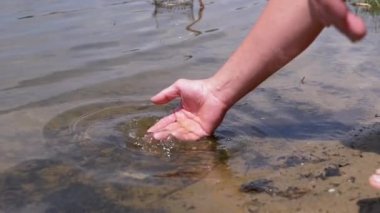 Male Hand Splashing in the Water, playing, creating Splashes in Sun at Sunset. Fingers touching surface of water. Drops are reflected in bright rays of sunlight. Concept of travel, enjoying nature.