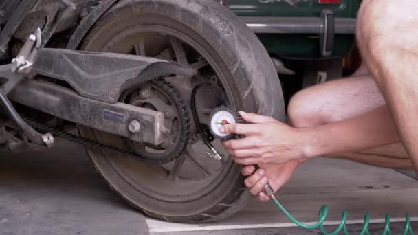 人は圧力計とオートバイのタイヤの空気圧を点検する 圧力計の針はタイヤの圧力を測定します 出発前に自動二輪車の安全性を確認するガレージ内のドライバー — ストック動画