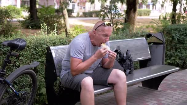 Голодный Велосипедист Отдыхает Скамейке Запасных Ест Хлеб Пита Улице Парке — стоковое видео