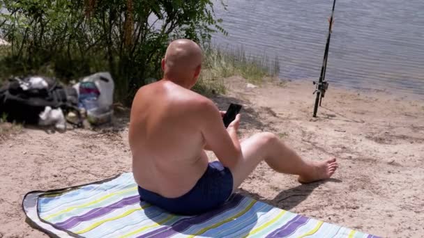 Gelooide Kale Man Holding Smartphone Handen Het Strand Zittend Een — Stockvideo