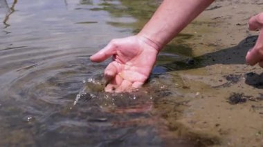 Male Hand Splashing in the Water, playing, creating Splashes in Sun at Sunset. Fingers touching surface of water. Drops are reflected in bright rays of sunlight. Concept of travel, enjoying nature.