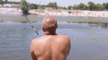 Angler Standing on Riverbank, Catching Fish, Looking into the Distance on Sunset. Back view of a bald man enjoying a fishing trip. Leisure, hobby, lifestyle. Nature, summer landscape. Weekend.