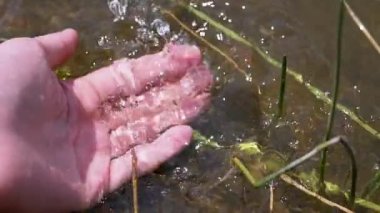 Female Hand Splashing in the Water, playing, creating Splashes in Sun at Sunset. Fingers touching surface of water. Drops are reflected in bright rays of sunlight. Concept of travel, enjoying nature.