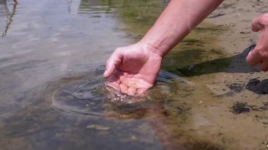 Male Hand Splashing in the Water, playing, creating Splashes in Sun at Sunset. Fingers touching surface of water. Drops are reflected in bright rays of sunlight. Concept of travel, enjoying nature.