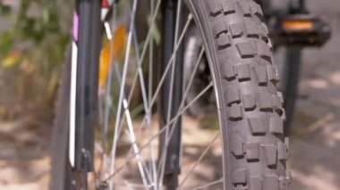 Modern Sports Bike Standing near a Tree in Forest in Windy Sunny Weather. Close-up of a spoked bicycle front wheel. Leafy forest. Sand. Concept sports, recreation, tourism, weekend, active lifestyle.