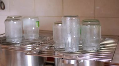 Sterilization of Glass Jars with Hot Steam on a Metal Grate at Home in Kitchen. Drops of water flowing down. Process of preparing glass containers for the preservation of vegetables for the winter.