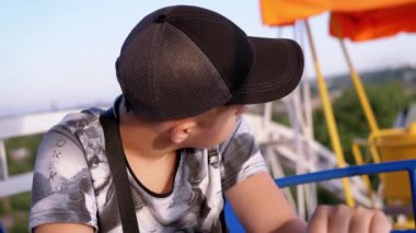 Smiling Boy Enjoying Panoramic View of the City from the Cabin of a Ferris Wheel. Happy child is worried, looking from a height at the sky, around, examining the surroundings, scenery. Amusement park.