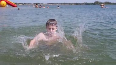 Happy Child Swimming, Splashing, Diving Underwater on the Beach in Sunlight. Boy hits the surface of the water with hands, creates splashes. Family vacation, resort. Recuperation, enjoyment. Summer.