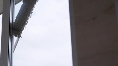 A Man Washing Windows on a Balcony with a Mop and Microfiber Cloth. A cleaner cleaning a dirty window on a blurred background of green trees. Cleaning service. Housekeeping. Housework. Close up.