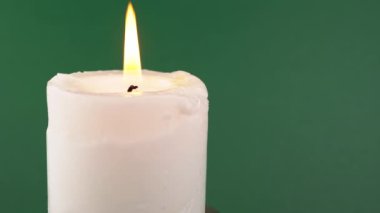 İzole edilmiş yeşil bir arka planda parlak bir alevle yanan beyaz mum. Parlak, sarı, sakin ateş. Hafıza kavramı, ritüel, kutlama. Soyut arkaplan, doku, renk. Yavaş çekim. Yakın plan..