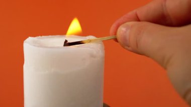 El Işıkları Beyaz Balmumu Mumunu Turuncu Arkaplanda Kibrit kullanarak. Parlak bir alev, ateş, karanlık bir odada ateşleme. Soyut arkaplan, doku, renk. Hafıza kavramı, ritüel, kutlama. Yakın plan..