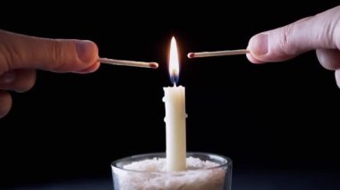 Hands Light a Two kibrit on a Flame Burning Candle on a Black Faground. Işık, parlak alev, ateş, karanlık bir odada duman. Soyut arkaplan, doku. Hafıza kavramı, ritüel, kutlama.