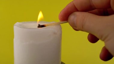 El Işıkları Beyaz Balmumu Mumunu Sarı Arkaplanda kibrit kullanarak yakar. Parlak bir alev, ateş, karanlık bir odada ateşleme. Soyut arkaplan, doku, renk. Hafıza kavramı, ritüel, kutlama. Yakın plan..