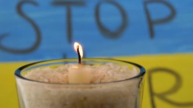Burning White Candle Against the Background of the Yellow Blue Flag of Ukraine. Inscription Stop the war on the national flag. Memory of the victims of the war, died soldiers in battle for Ukraine.
