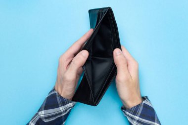 Mavi arka planda boş bir cüzdan tutan genç adam. Finansal okuryazarlık. İflas etti. Para sıkıntısı var. Tasarrufların önemi.