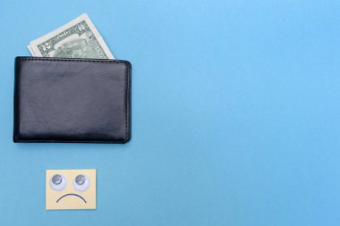 Cüzdanda iki dolar var. Mesajın için yer aç. Uzayı kopyala Üzgün tebessüm cüzdana bakıyor. Mavi arka plan. İflas etti. Para sıkıntısı var. Birikimlerin önemi. Mali yardım kavramı.