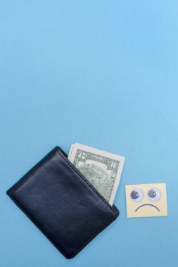 Cüzdanda iki dolar var. Mesajın için yer aç. Uzayı kopyala Üzgün tebessüm cüzdana bakıyor. Mavi arka plan. İflas etti. Para sıkıntısı var. Birikimlerin önemi. Mali yardım kavramı. Dikey.