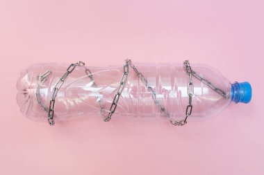 Pembe arka planda zincirli boş plastik şişe. Su kıtlığı ve kuraklık kavramı. Suyun büyük değeri. Düz yatıyordu.