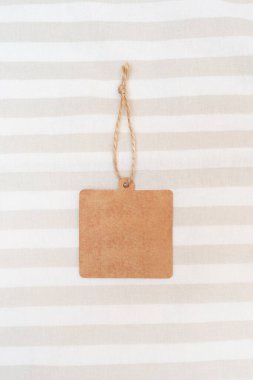 Boş kare etiket, kahverengi kağıt etiket yatak örtüsünün üzerinde. El işi karton etiket. Uzayı kopyala Mesaj ve şirket logosu için yer. Modelleme. Üst manzara, düz uzanma