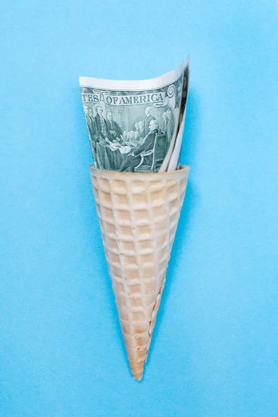 Ice cream cone and American US dollars on a blue background. Waffle cone. Finance. Inflation. Money is tight. Vertical. Flat lay