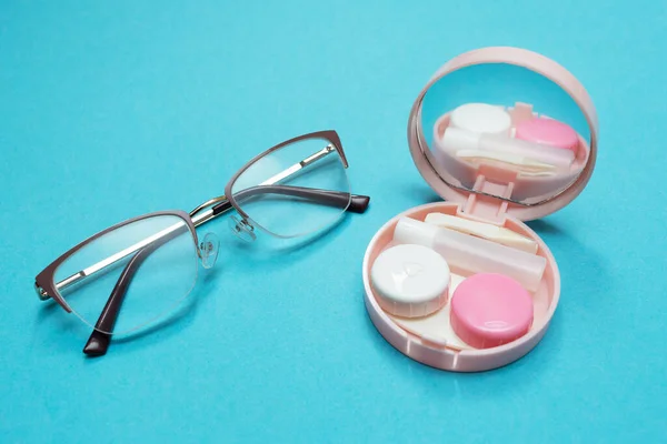 Glasses and travel kit for contact lenses on a blue background. Choosing between glasses and lenses. Caring for vision health. Myopia and eyesight problem concept Лицензионные Стоковые Фото