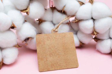 Kağıt boş etiketi kahverengi ve pamuk çiçekleri pembe arka planda. Boş kare etiket. Mesaj ve şirket logosu için yer. Tasarım için tasarım. Uzayı kopyala Yakın çekim.