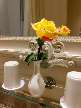 Banyodaki beyaz vazoda sarı ve pembe bir gül.