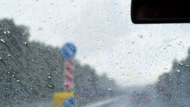 Arabadan bak. Yağmurlu hava nedeniyle ıslak ön cam. Şiddetli yağmur yağsa bile yol işaretleri açıkça görülebilir..