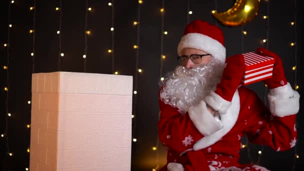 Jultomten skakar julklapp låda och sätter den i huset skorsten. — Stockvideo