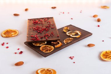 İki doğal organik acı çikolata, süblimleşmiş böğürtlen, turuncu ve fındıklı beyaz arka plan. Şekerleme malzemeleri. Yan görünüm.