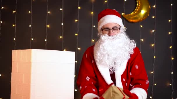 Santa vyhazuje vánoční dárky do vzduchu a dává je do komína domu. — Stock video