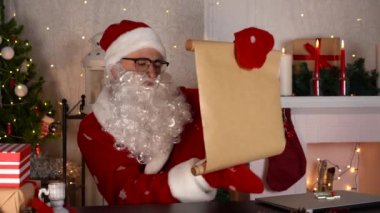 Geleneksel Noel Baba, şöminenin yanındaki hediye kutularıyla istek listesini kontrol ediyor. 