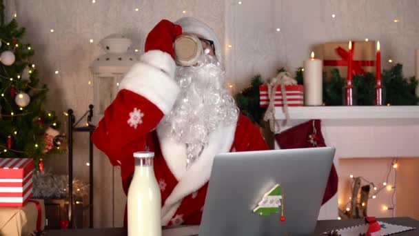 Der Weihnachtsmann in seiner Weihnachtswerkstatt mit Laptop und leckerer Milch. — Stockvideo