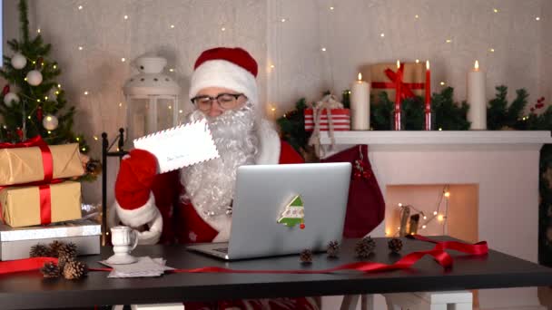 Święty Mikołaj siedzi w swoim domu warsztatowym, czytając list za pomocą laptopa — Wideo stockowe