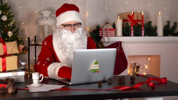 Der Weihnachtsmann bereitet Weihnachtsgeschenke vor. Er zählt Kisten und tippt auf einem Laptop. — Stockvideo