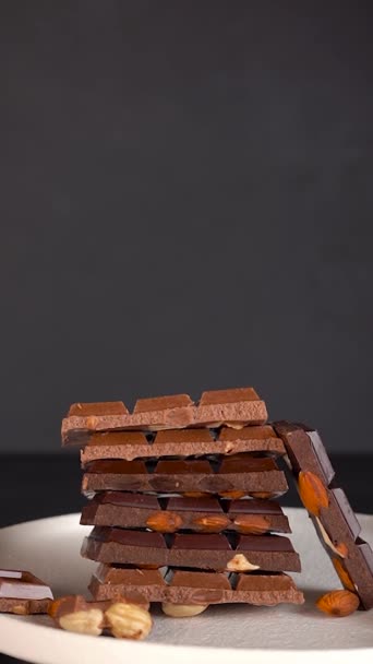 Растаянный шоколад льется на тарелку с кусочками шоколада с орехами. Медленно — стоковое видео