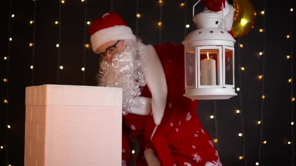 Papai Noel olha dentro da chaminé da casa com lâmpada de vela na noite de Natal. — Vídeo de Stock