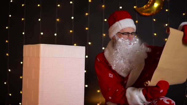 Père Noël lire la liste de souhaits près de la cheminée de la maison sur le toit, nuit de Noël. — Video