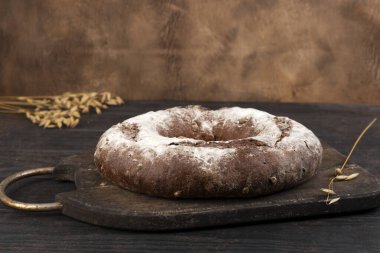 Ev yapımı mayalı ekmek, arka planda çavdar unu ve çavdar kulağı. Yan görünüm.