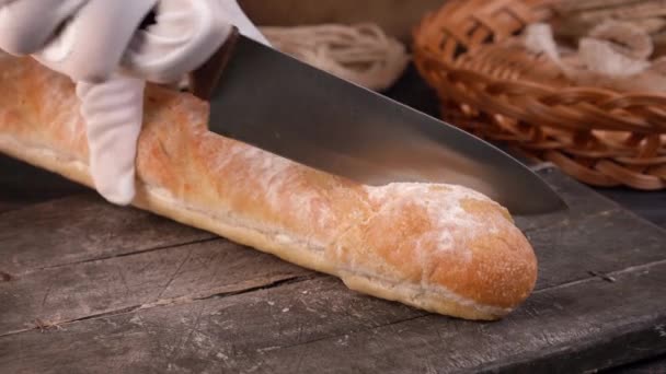 The chef cuts homemade crispy baguette bread into slices with kitchen knife. — Stock Video