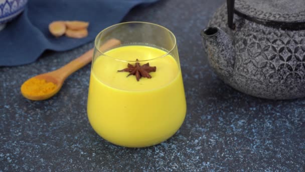 スターアニーズは、ターメリックゴールデンムーンミルクのガラスの中で回転しています。健康飲料. — ストック動画