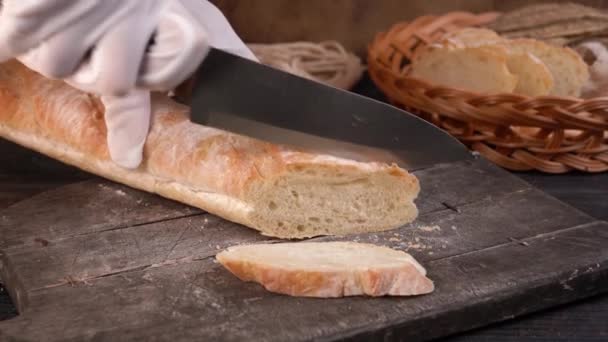 The chef cuts fresh crispy baguette into slices with kitchen knife. Close-up. — Stock Video