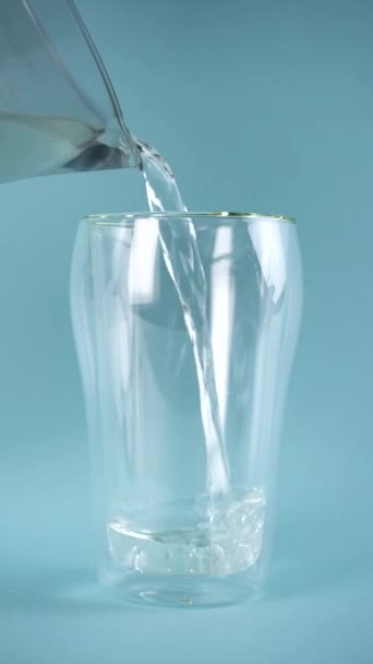 Zoet water wordt in een dubbelwandig glas gegoten. Langzame beweging. Verticaal. — Stockvideo