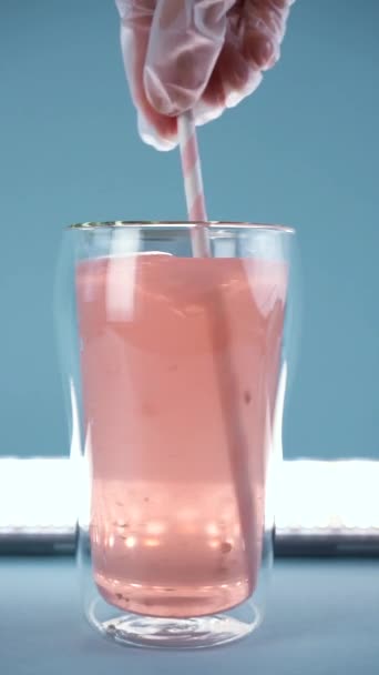 Das Kollagen in einem Glas Wasser mit einem rosa Trinkhalm verrühren. Zeitlupe. — Stockvideo