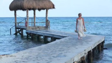 Bir kadın tropik tatil köyünde iskelede yürüyor.