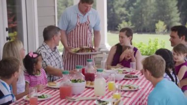 Bir grup insan arka bahçede barbekü yiyor ve eğleniyor.