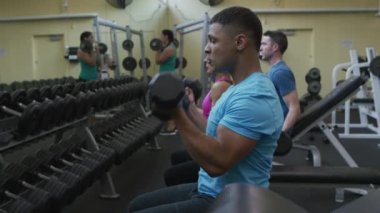 Spor salonunda insanlar ağırlık kaldırıyor.